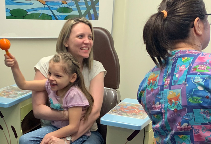 An FCDGC patient sits with their guardian and plays with a maraca during a doctor's office visit.